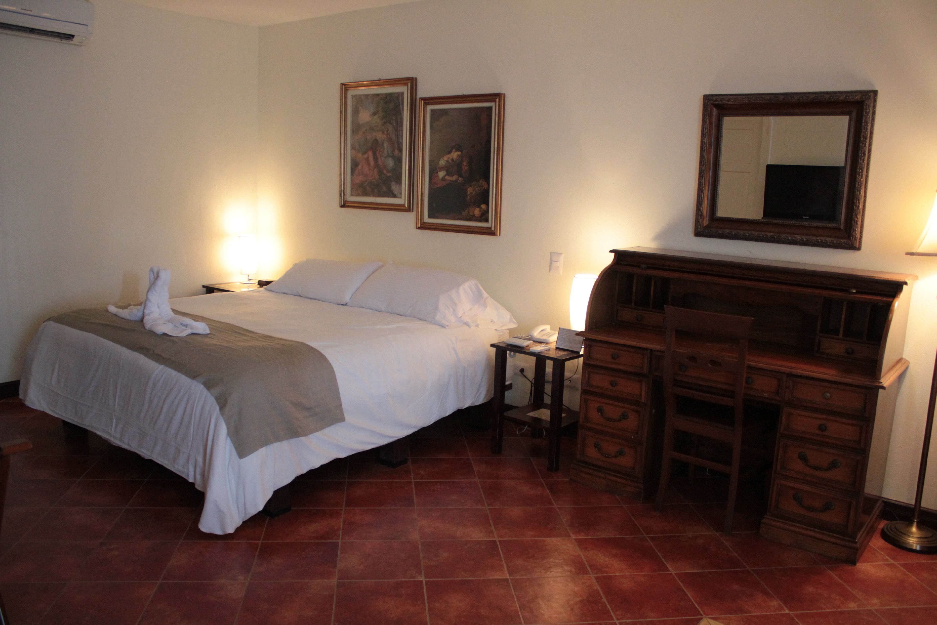 A hotel room with a bed, bedside tables, a dresser, and two framed pictures on the wall.