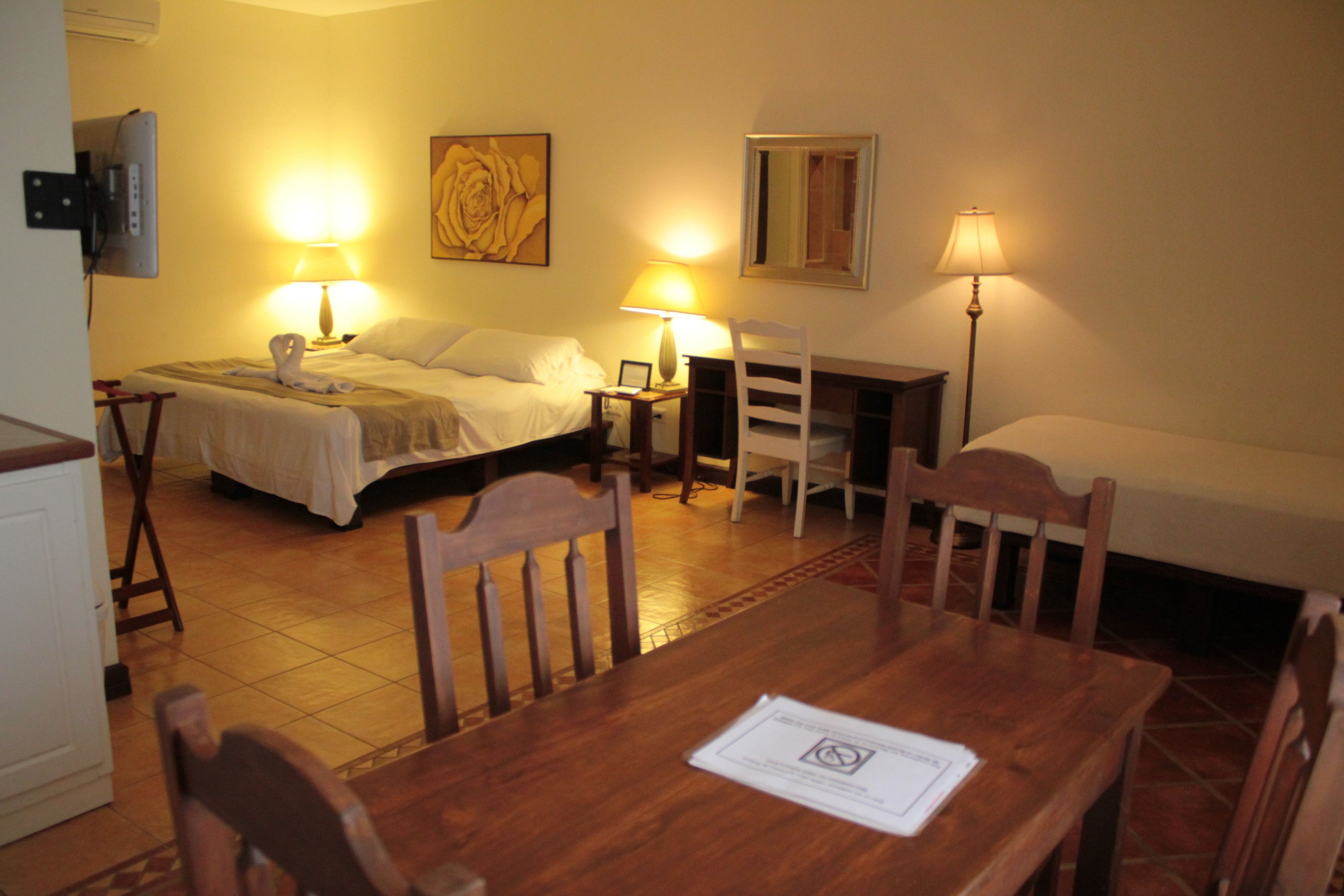 Une chambre d’hôtel comprenant un lit, deux tables de chevet, un bureau avec des chaises, une lampe et un tableau au mur.