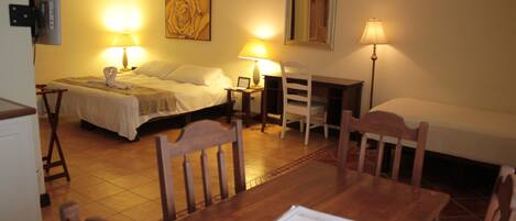 Une chambre d’hôtel comprenant un lit, deux tables de chevet, un bureau avec des chaises, une lampe et un tableau au mur.