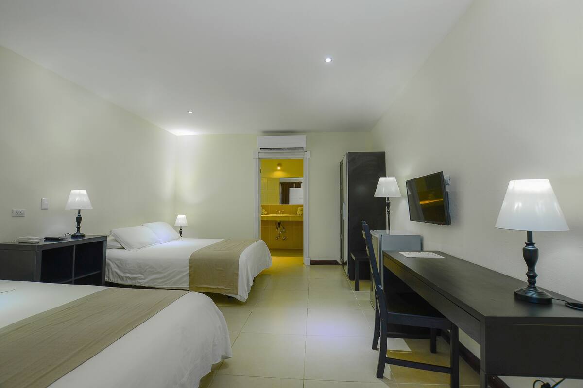 Ein Hotelzimmer mit zwei Betten, einem Schreibtisch, einem Stuhl, einem Fernseher und einem durch eine offene Tür einsehbaren Badezimmer.