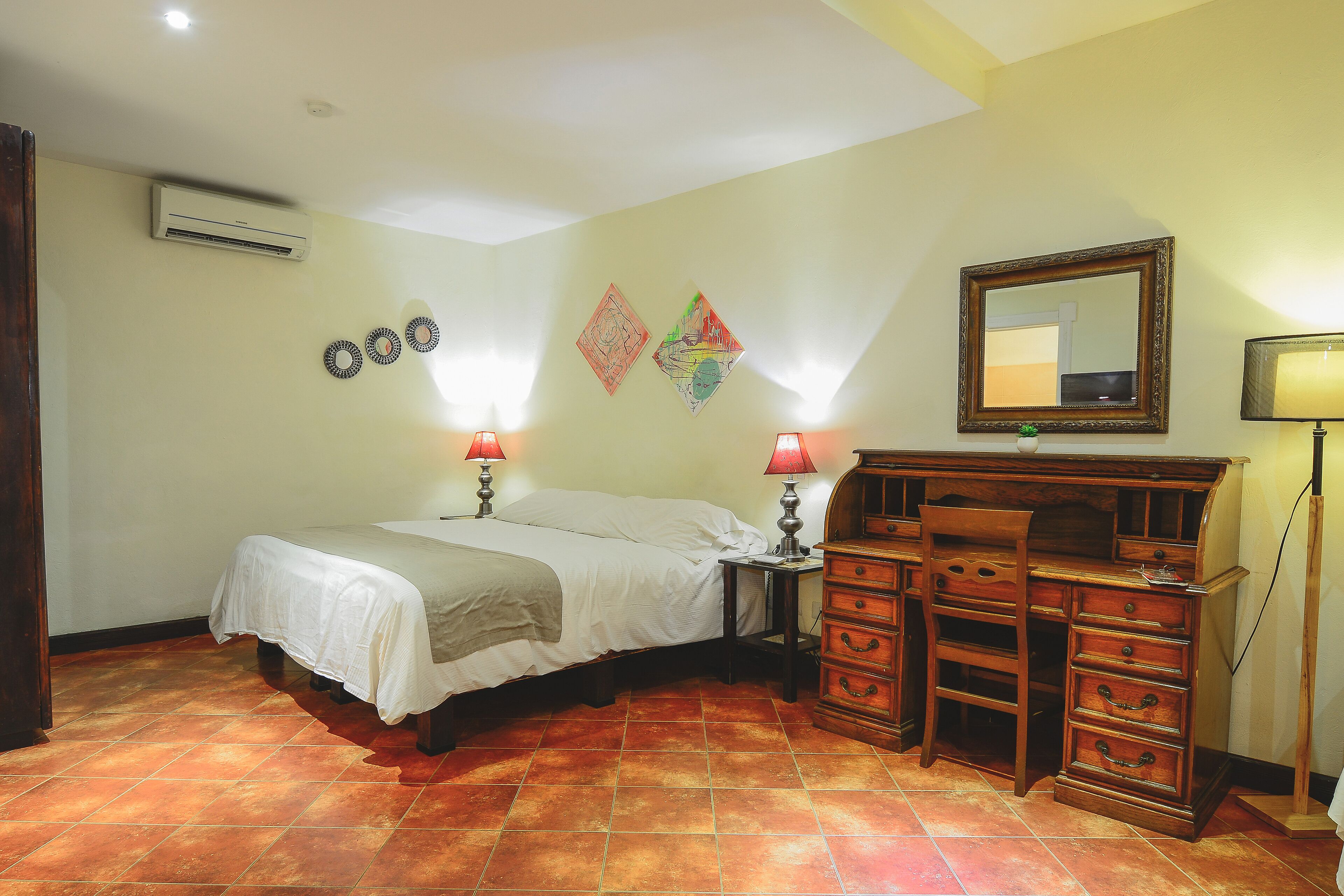 A bedroom with a bed, dresser, and wall-mounted mirror.