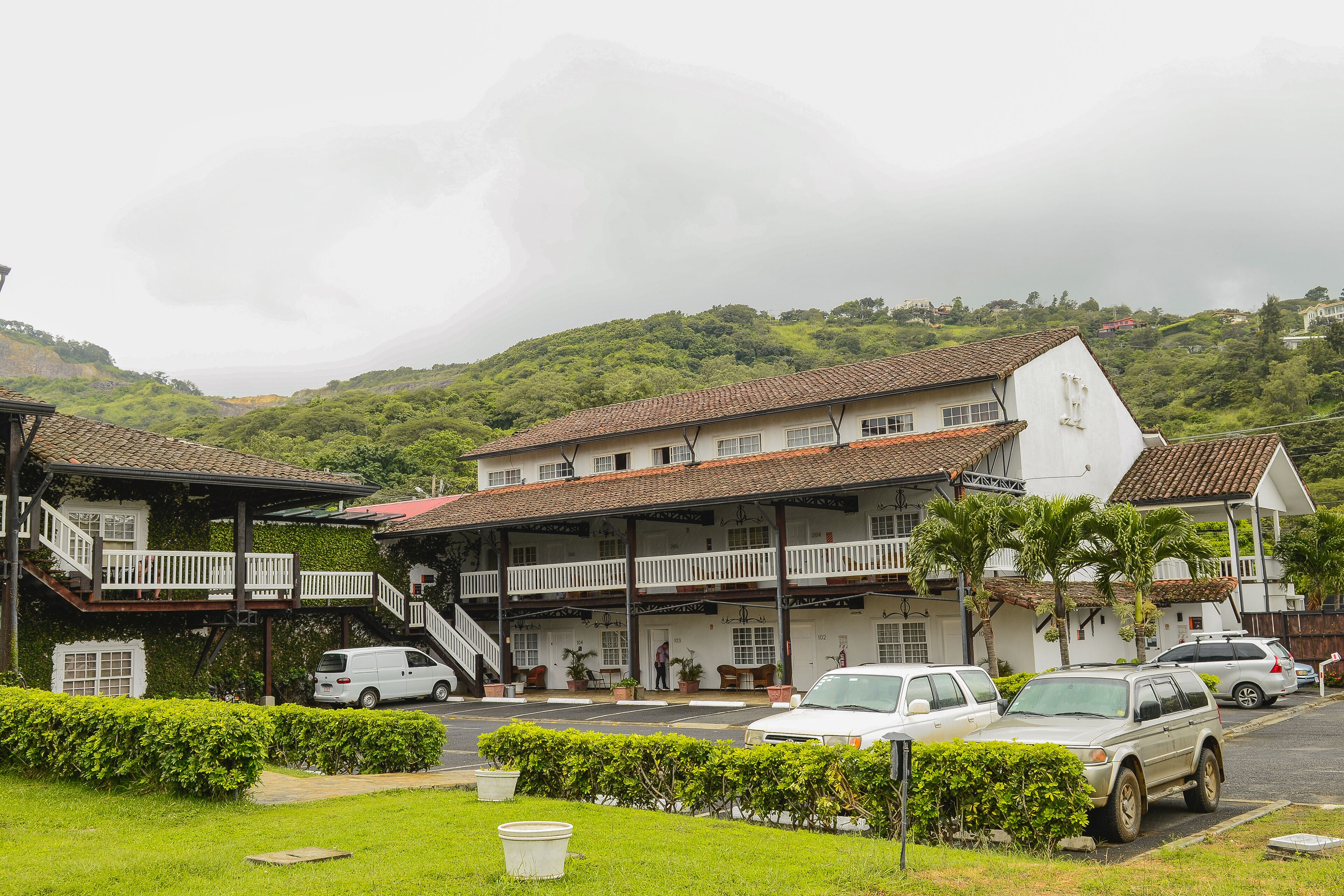 A two-story building with a balcony, a staircase, and a parking area with cars.