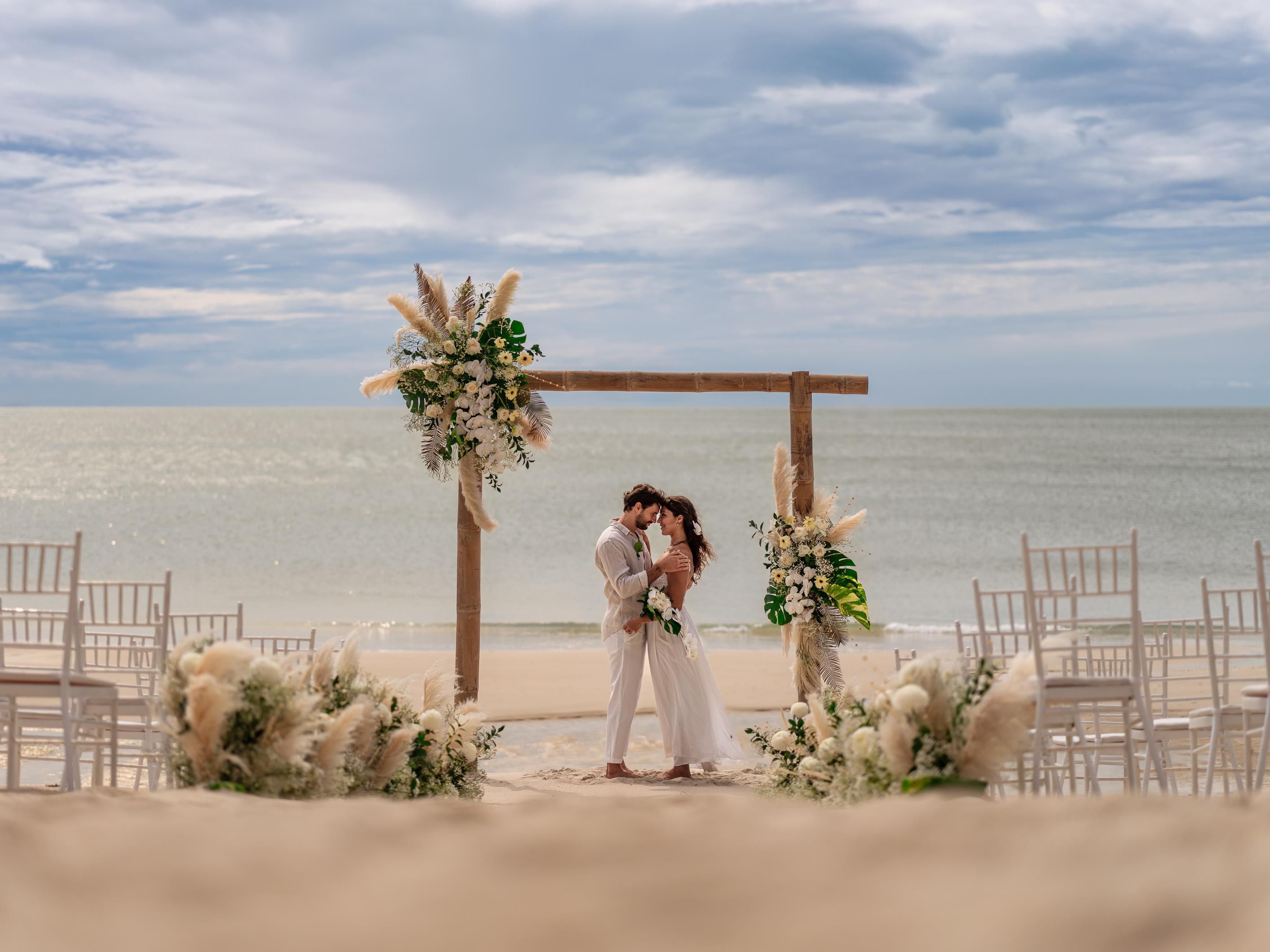 Ceremonia de boda en la playa con un arco de madera y decoración floral.