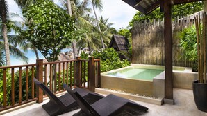 A poolside area with lounge chairs, a hot tub, and a view of palm trees and the ocean.