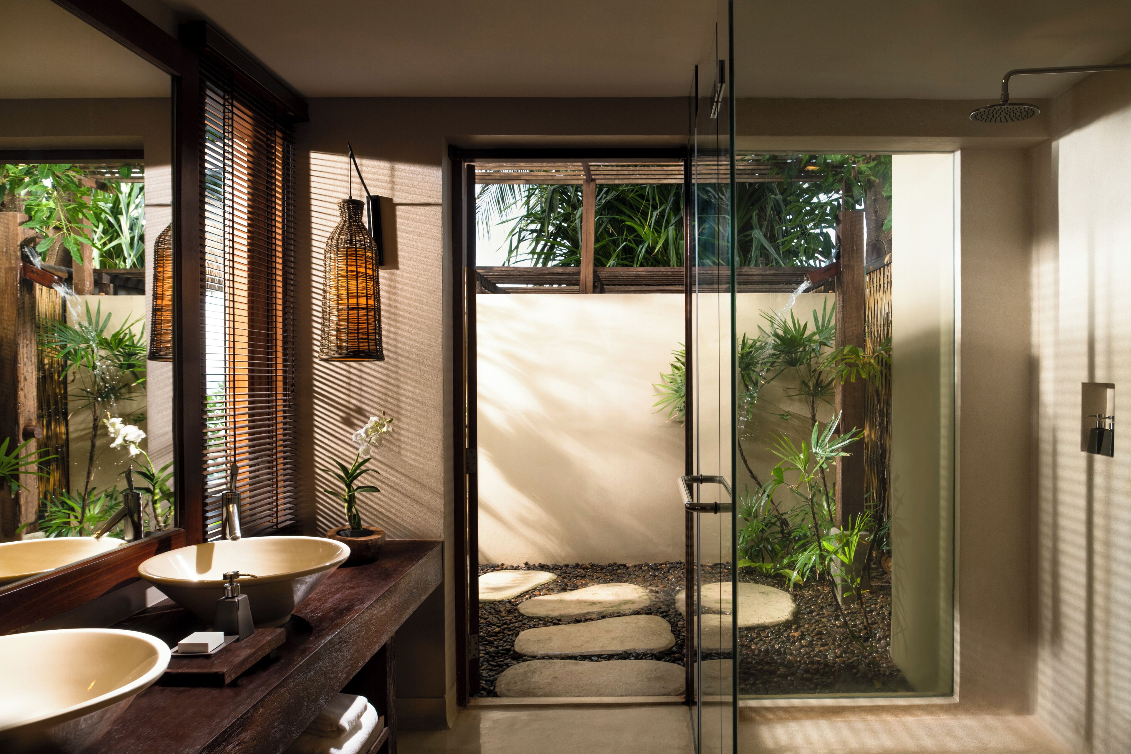 Un baño moderno con dos lavamanos grandes, una cabina de ducha con paredes de vidrio y un camino de piedra que conduce a un jardín.