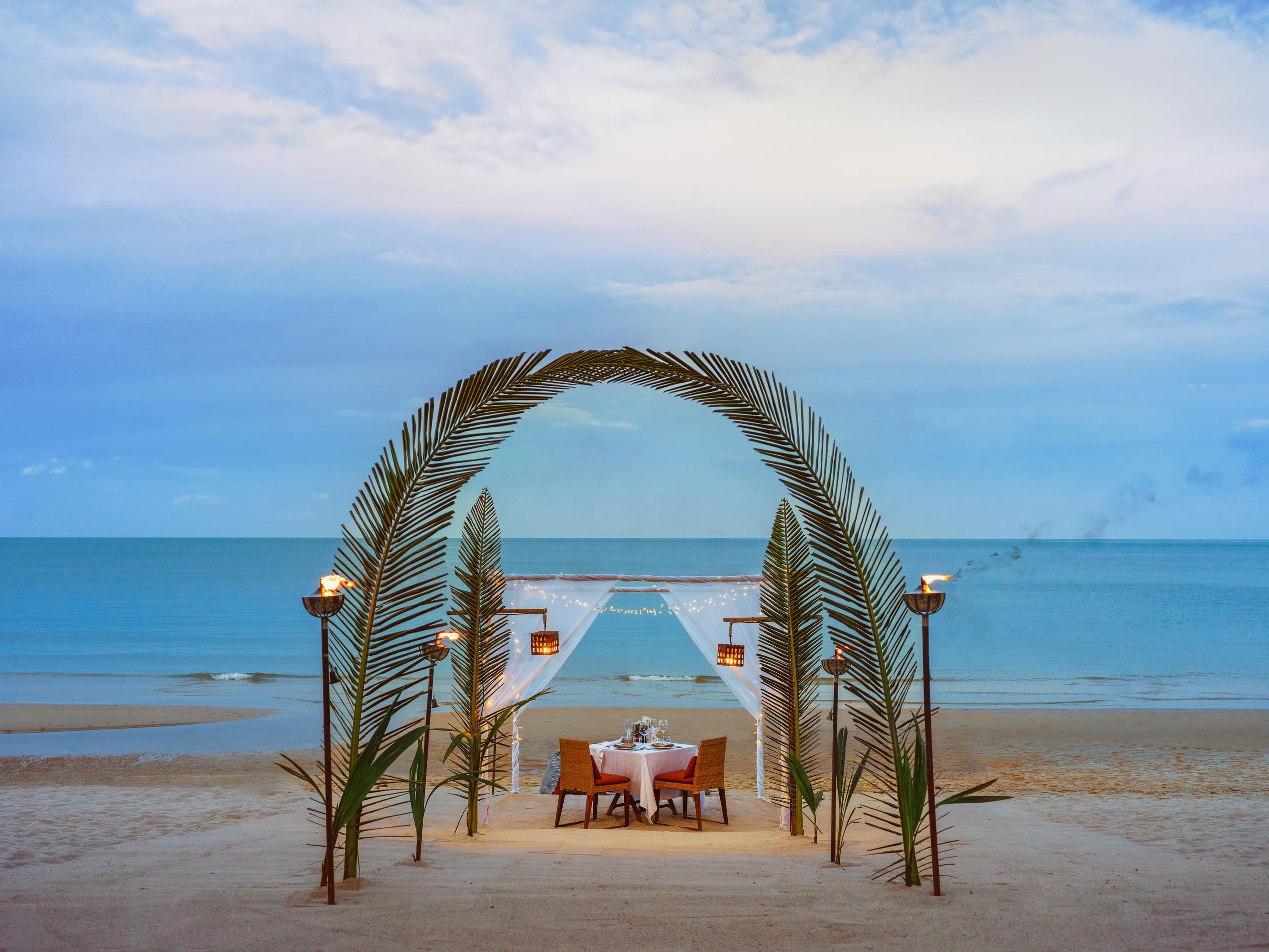 Decoración para una boda en la playa, con una carpa, sillas y una mesa.