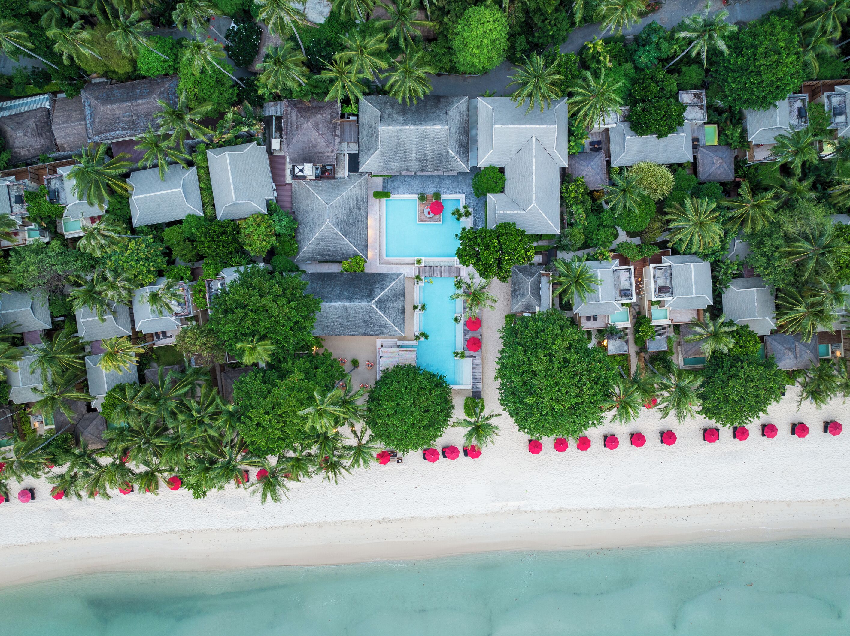Vista aérea de un resort con varias cabañas, una piscina central y acceso a la playa.