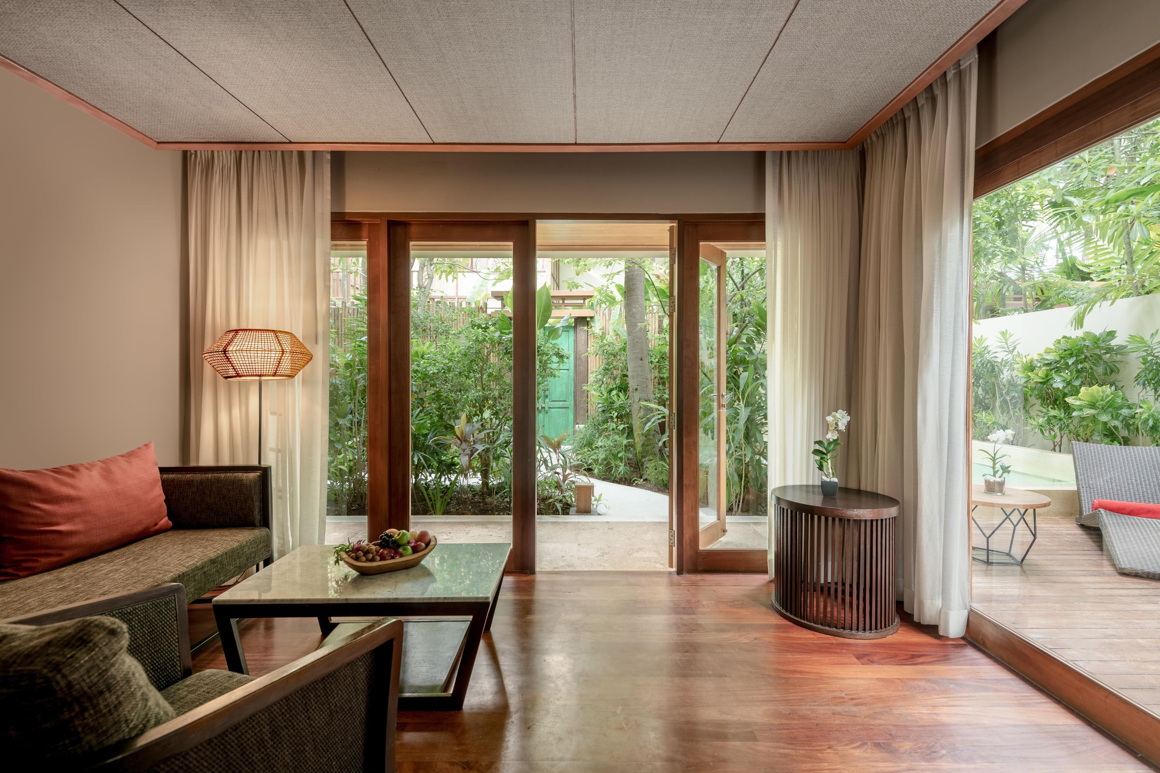 Sala de estar moderna com sofá, mesa de centro e vista para um jardim exuberante através de grandes portas de correr.