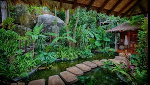 A lush indoor garden with a pond, stone steps, and a thatched-roof structure. - Anantara Rasananda Koh Phangan Villas (Ko Pha-ngan)