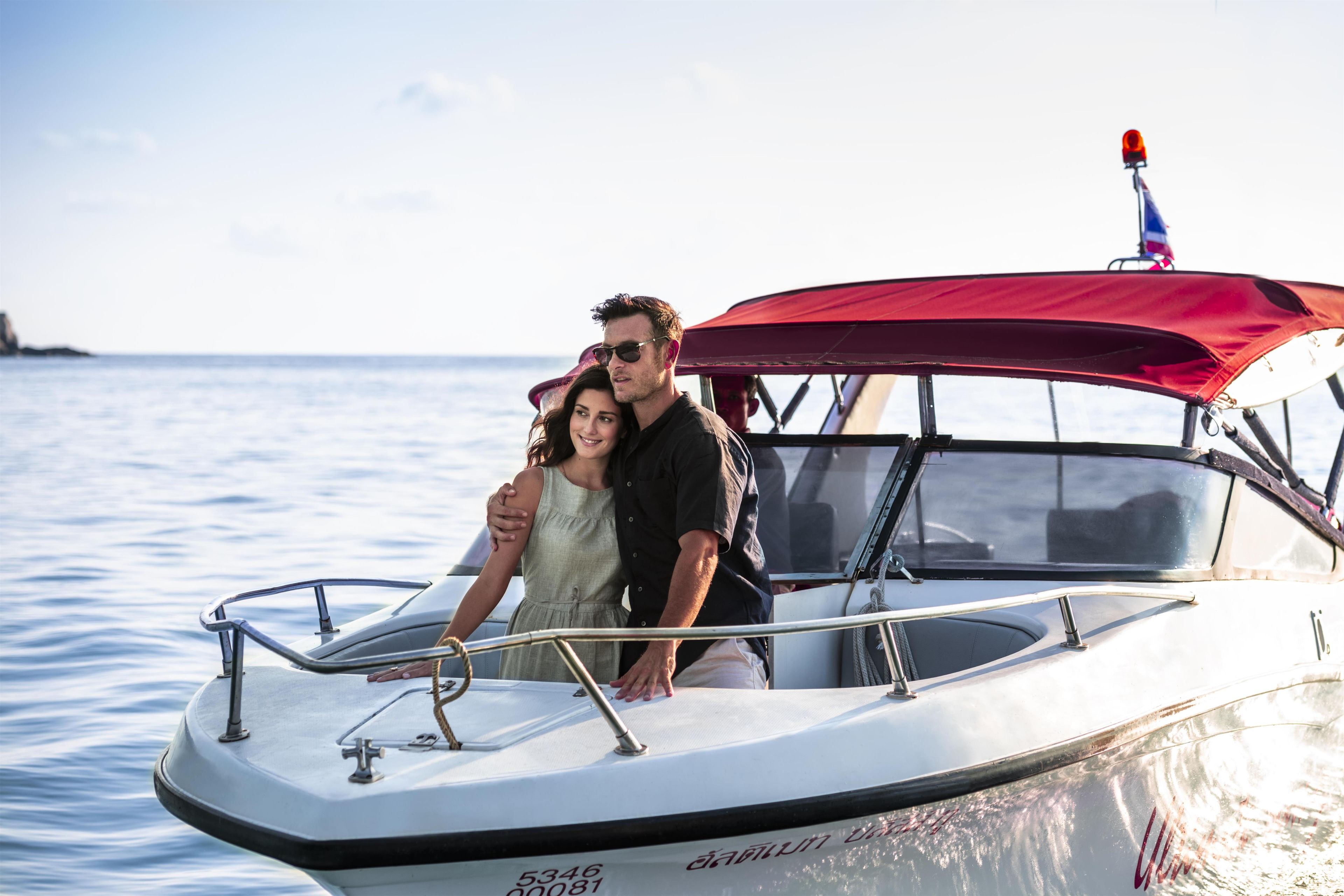 Un bateau avec un auvent rouge, une personne au volant et une autre personne assise à côté.