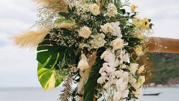 Um arco de casamento decorado com flores brancas e capim-do-campo, com o mar ao fundo.