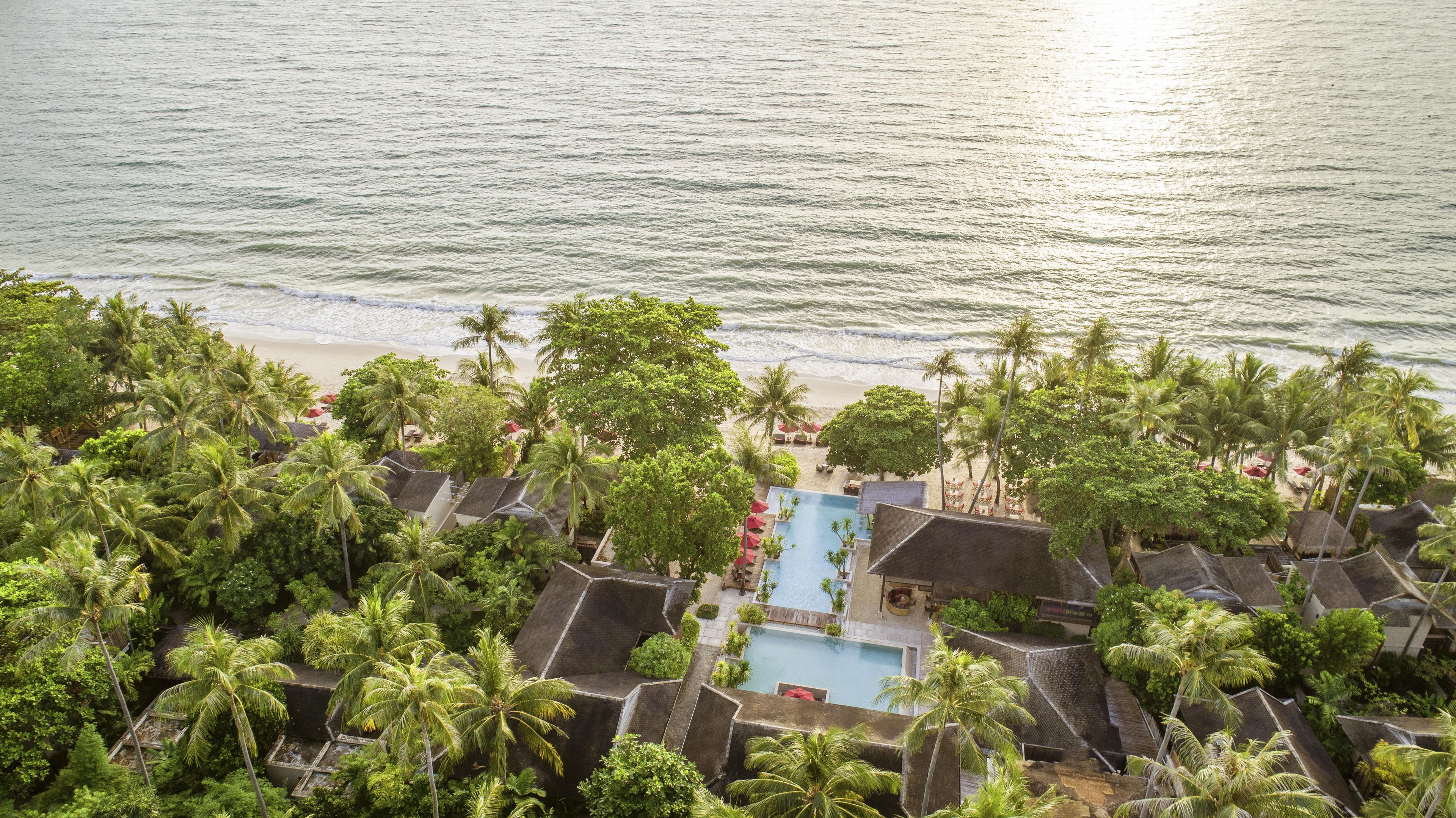 Un resort con piscina, palmeras y vistas a la playa.