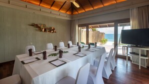 A conference room with a long table, white chairs, a ceiling fan, and a TV.