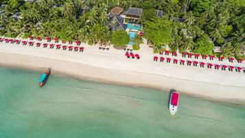 An aerial view of a beach resort with a swimming pool, lounge chairs, and boats.