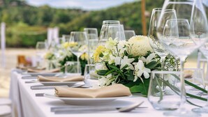 A table set for a formal outdoor event with white tablecloths, clear glassware, and floral centerpieces.
