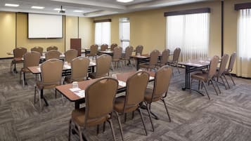 A conference room with multiple tables and chairs, a projector screen, and large windows with blinds.