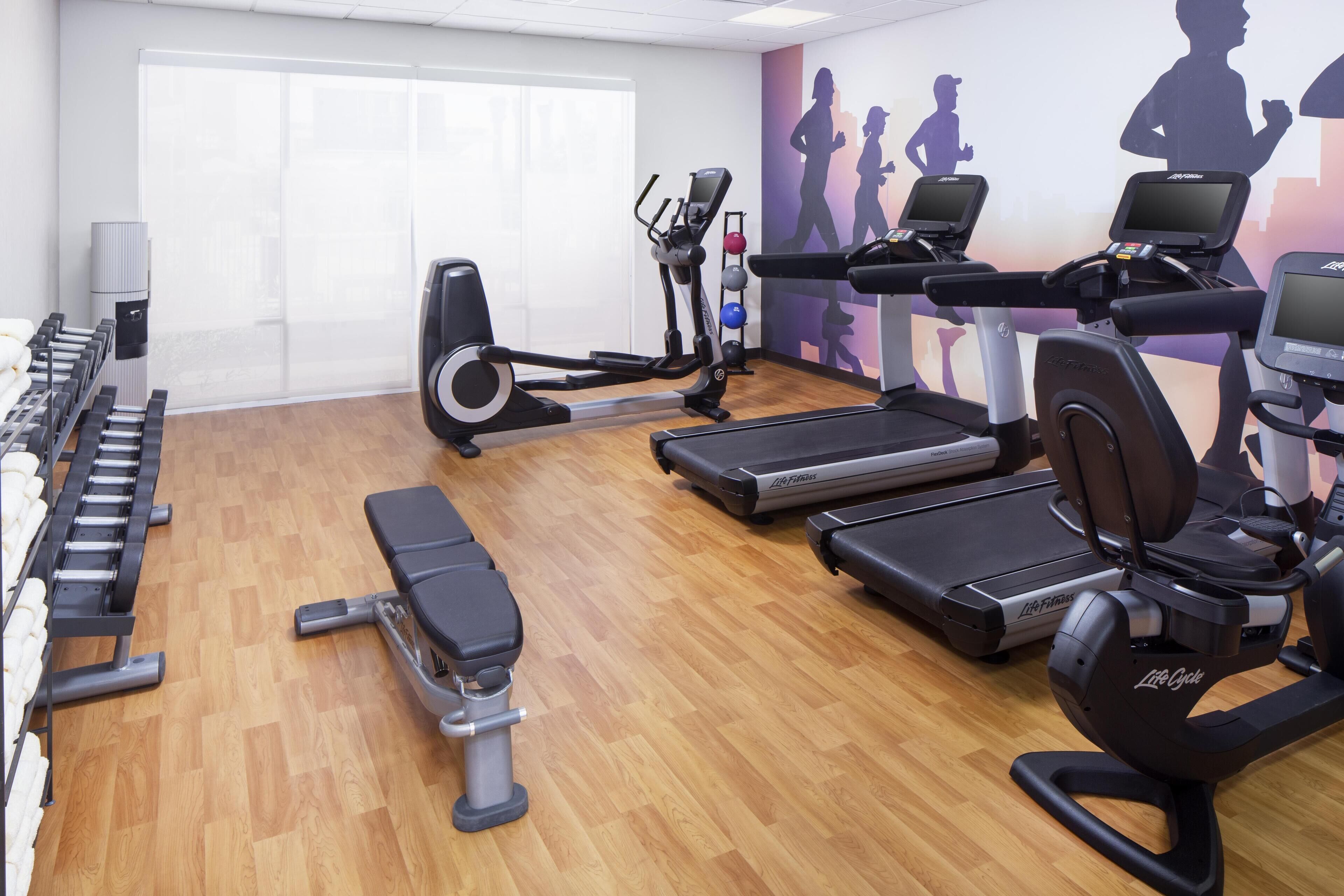 Ein Fitnessstudio mit Laufbändern, Crosstrainern und Gewichtsbänken.