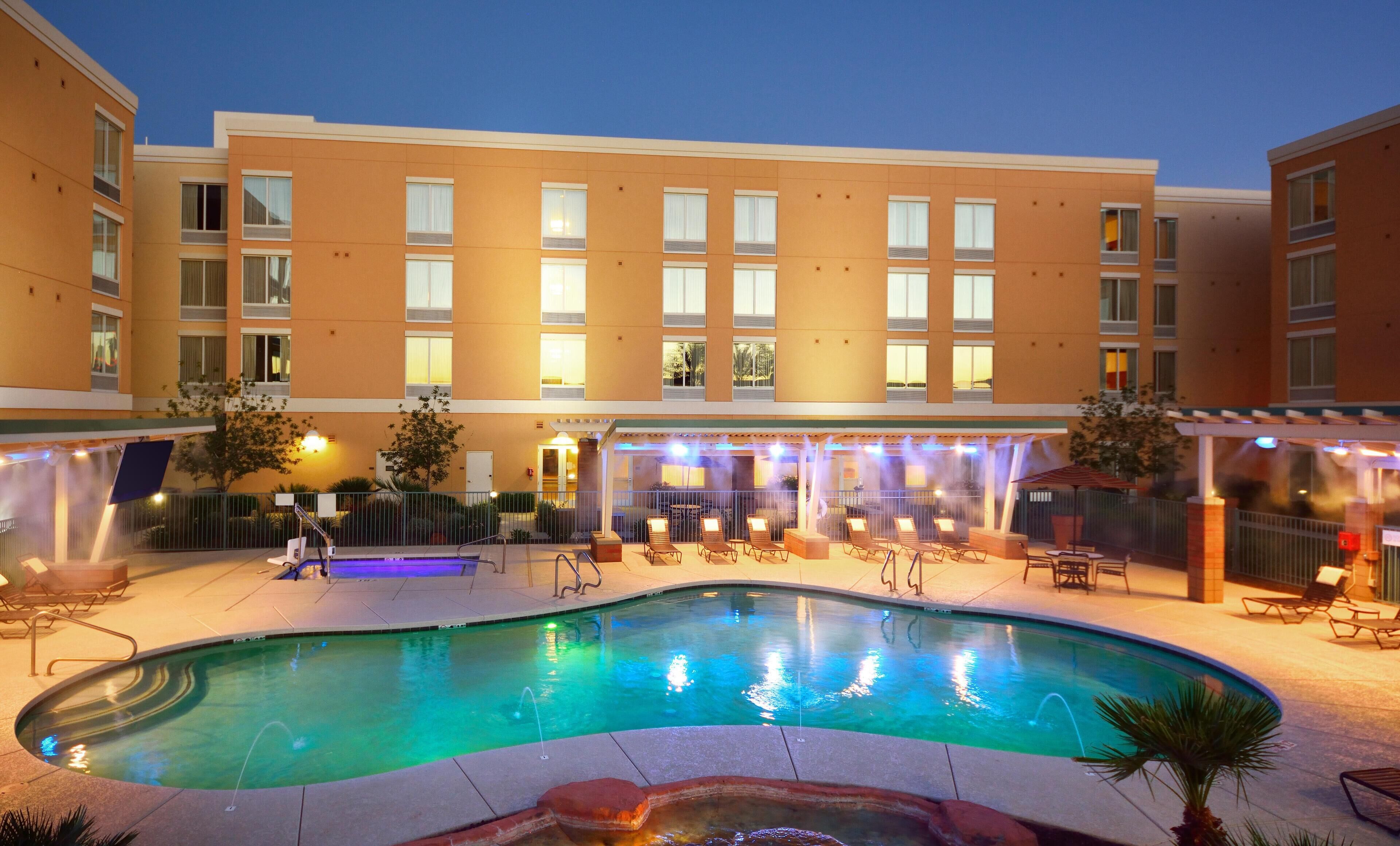 A hotel courtyard with a swimming pool, outdoor seating, and a covered patio area.
