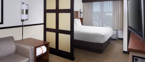 A hotel room with a bed, a sofa, a TV, and a partition wall.