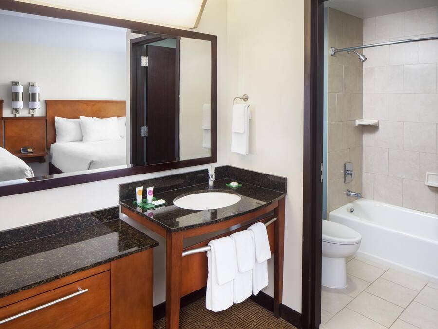 Un bany d'hotel amb un mirall gran, un lavabo, un vàter i una banyera.