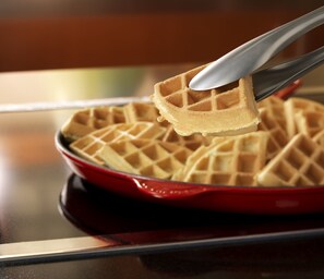 A waffle being lifted with tongs from a red waffle iron.