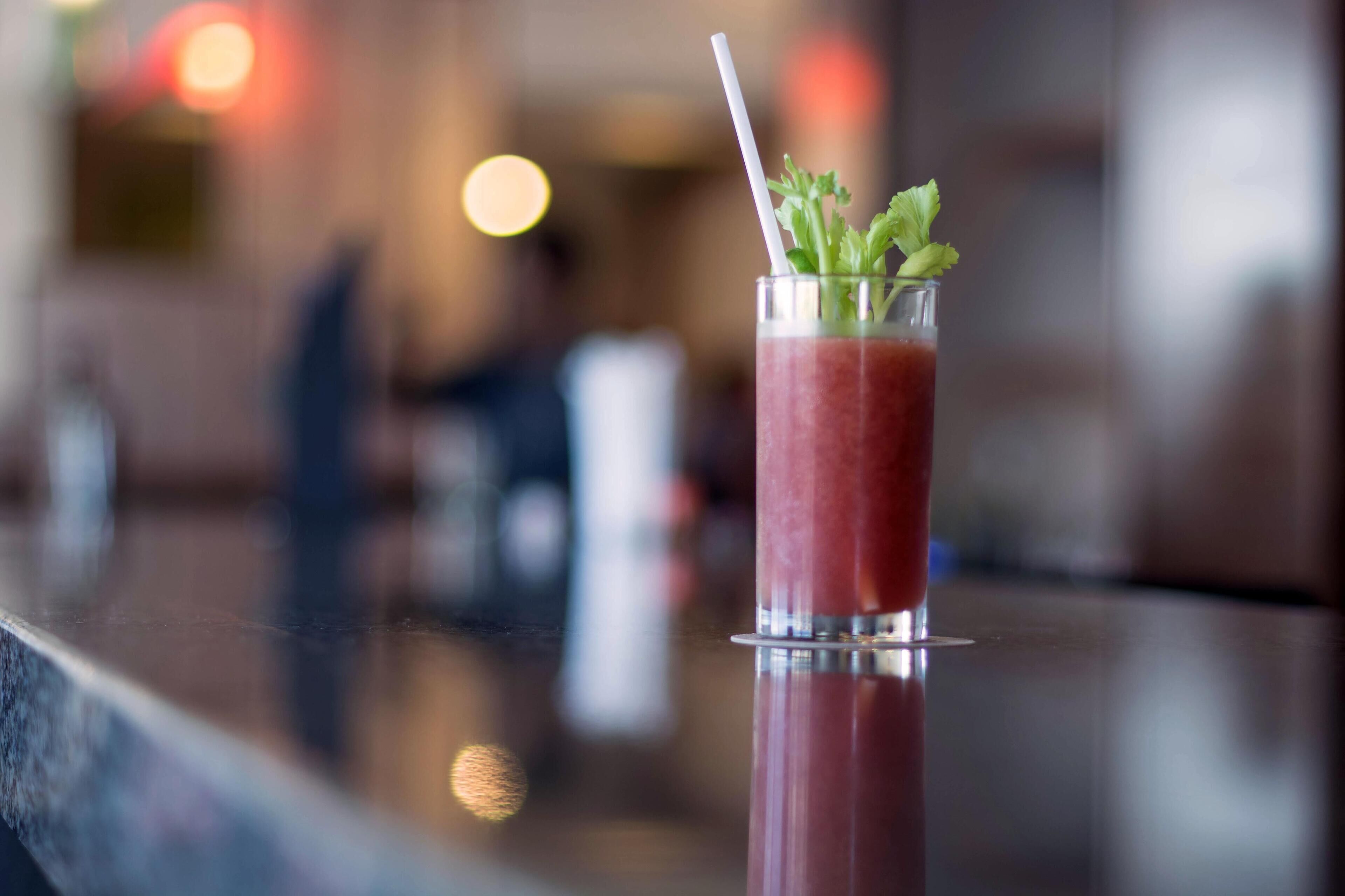 A glass of red drink with a straw and garnish on a reflective surface.