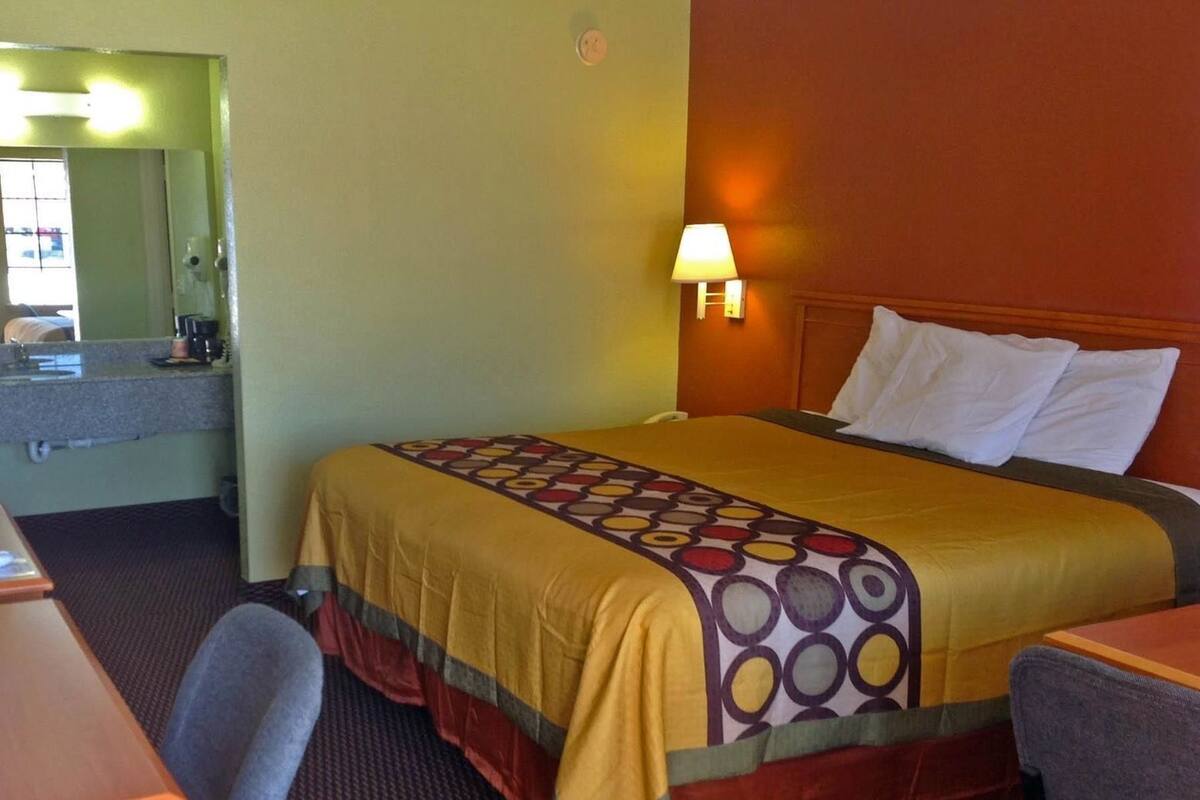 A hotel room with a bed, a desk, a chair, a lamp, and a mirror.