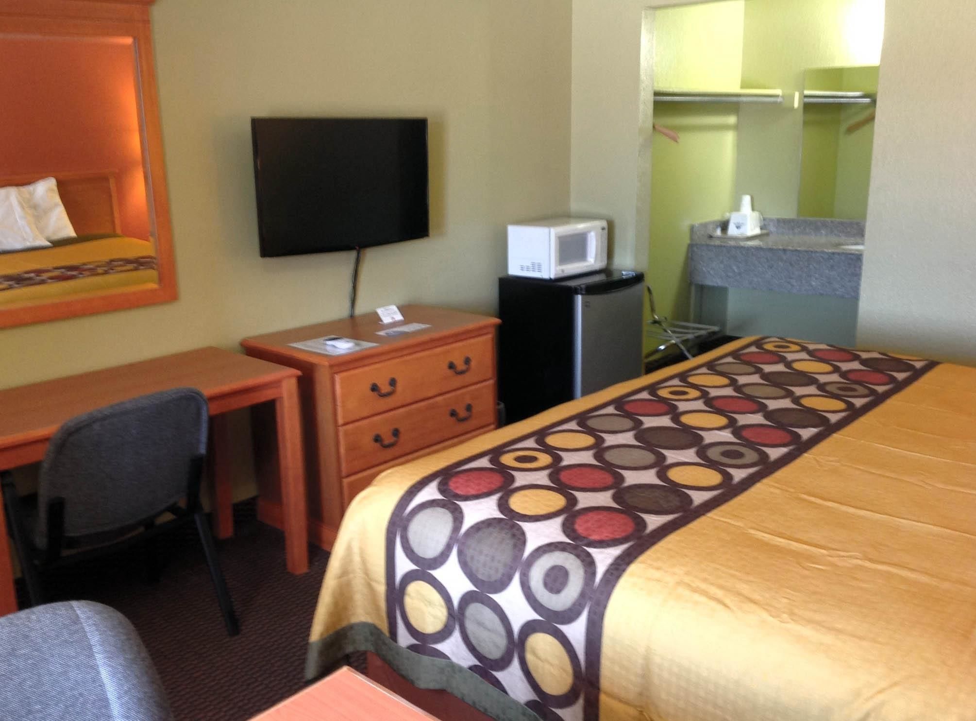 A hotel room with a bed, a desk, a chair, a television, a microwave, and a small kitchenette.