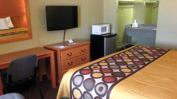 A hotel room with a bed, a desk, a chair, a television, a microwave, and a small kitchenette.
