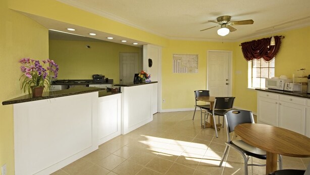 A bright kitchen with white cabinets, a dining area with a wooden table and chairs, a ceiling fan, and a window with curtains. - Americas Best Value Inn Pryor (Pryor)