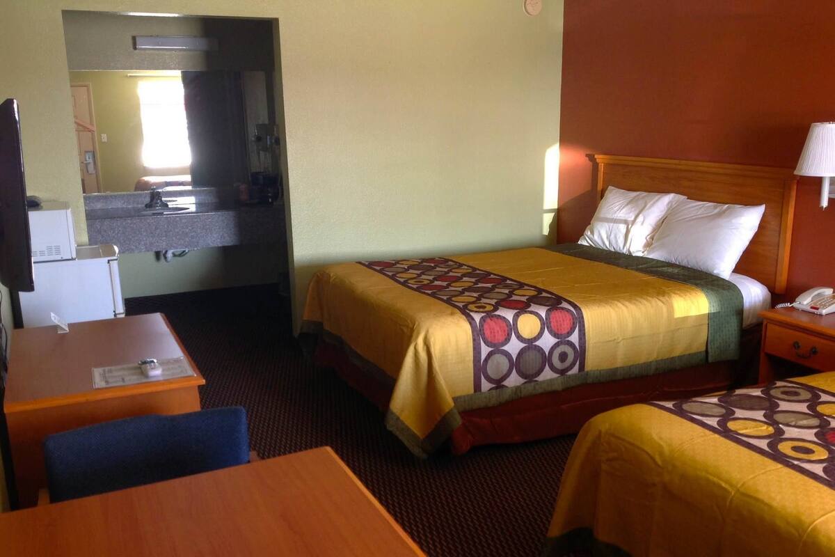 A hotel room with a bed, a desk, a chair, a nightstand, and a lamp.