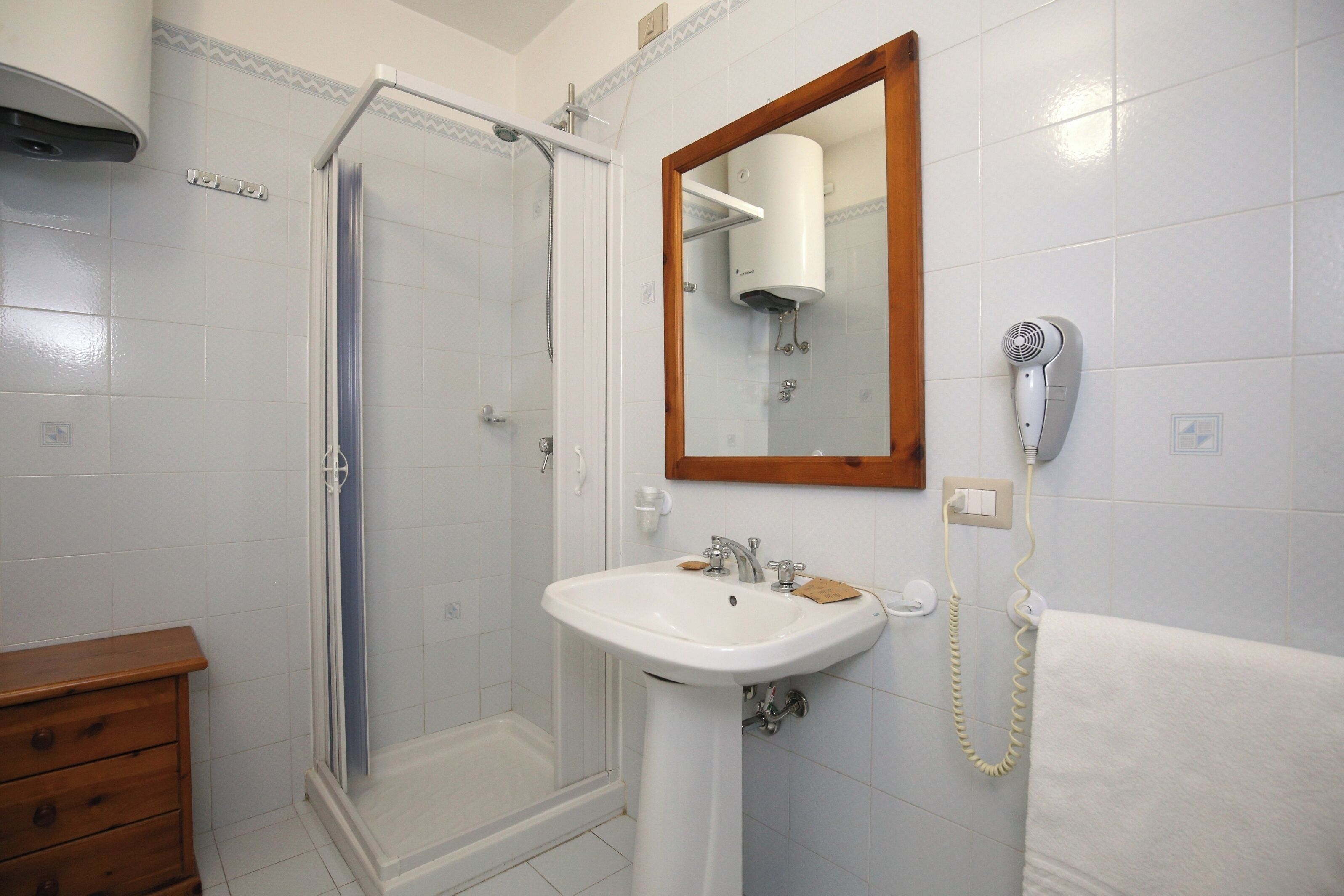 Ein Badezimmer mit Dusche, Waschbecken und einem an der Wand befestigten Föhn.