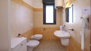Une salle de bain comprenant des toilettes, un bidet, un lavabo et une fenêtre.