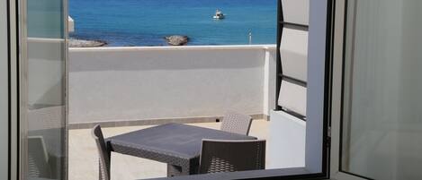 A balcony with a table and chairs, overlooking a clear blue sea with a boat in the distance.