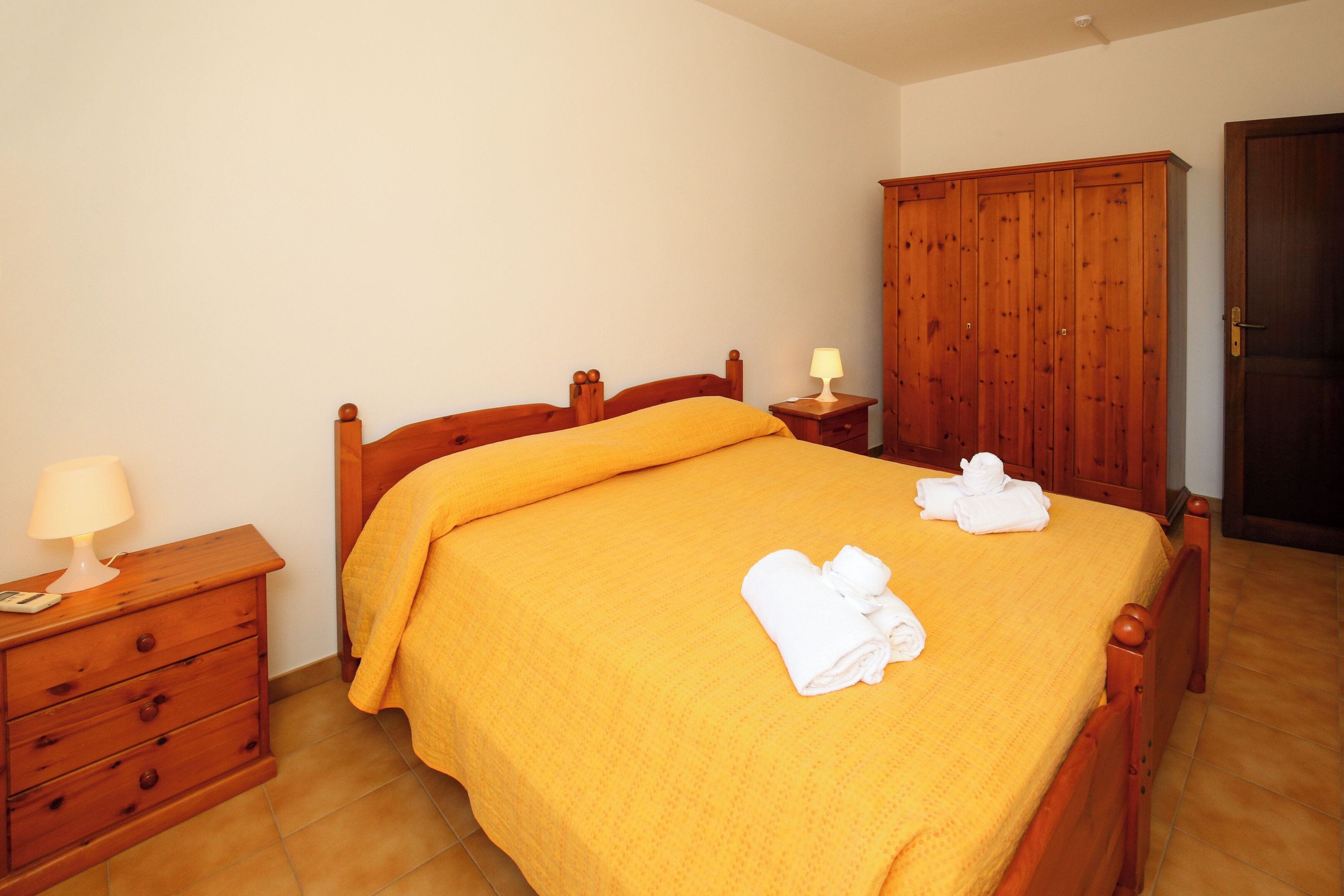A bedroom with a wooden bed, a nightstand, a lamp, and a wardrobe.