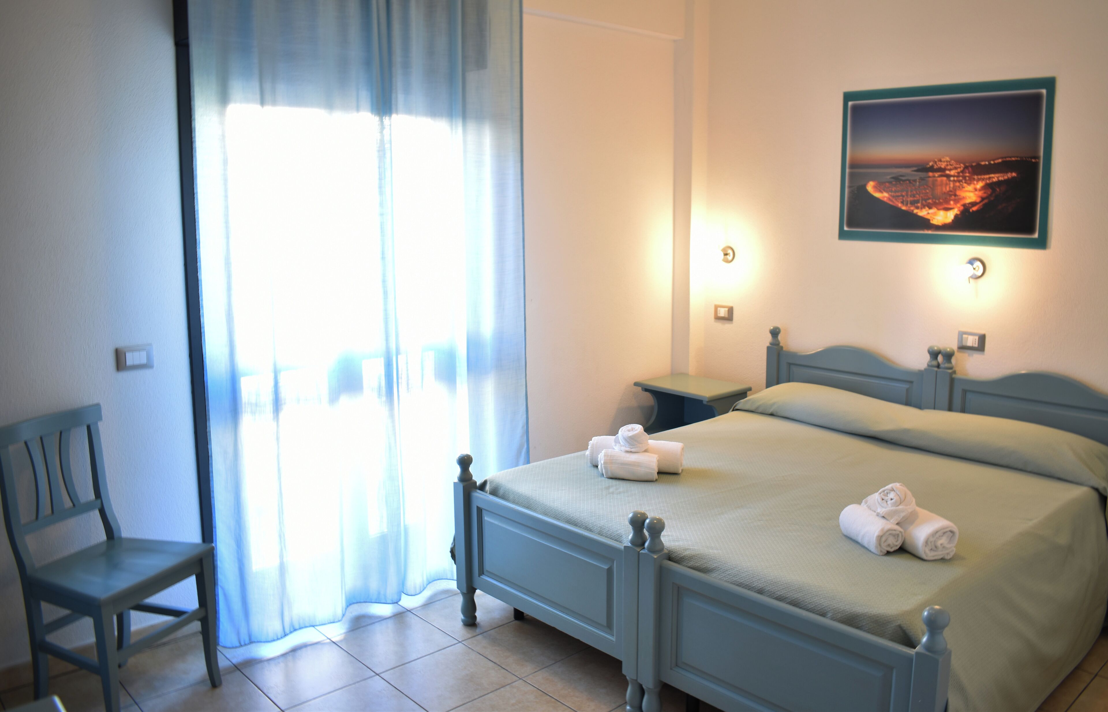 A bedroom with a bed, a chair, a nightstand, and a wall-mounted picture.