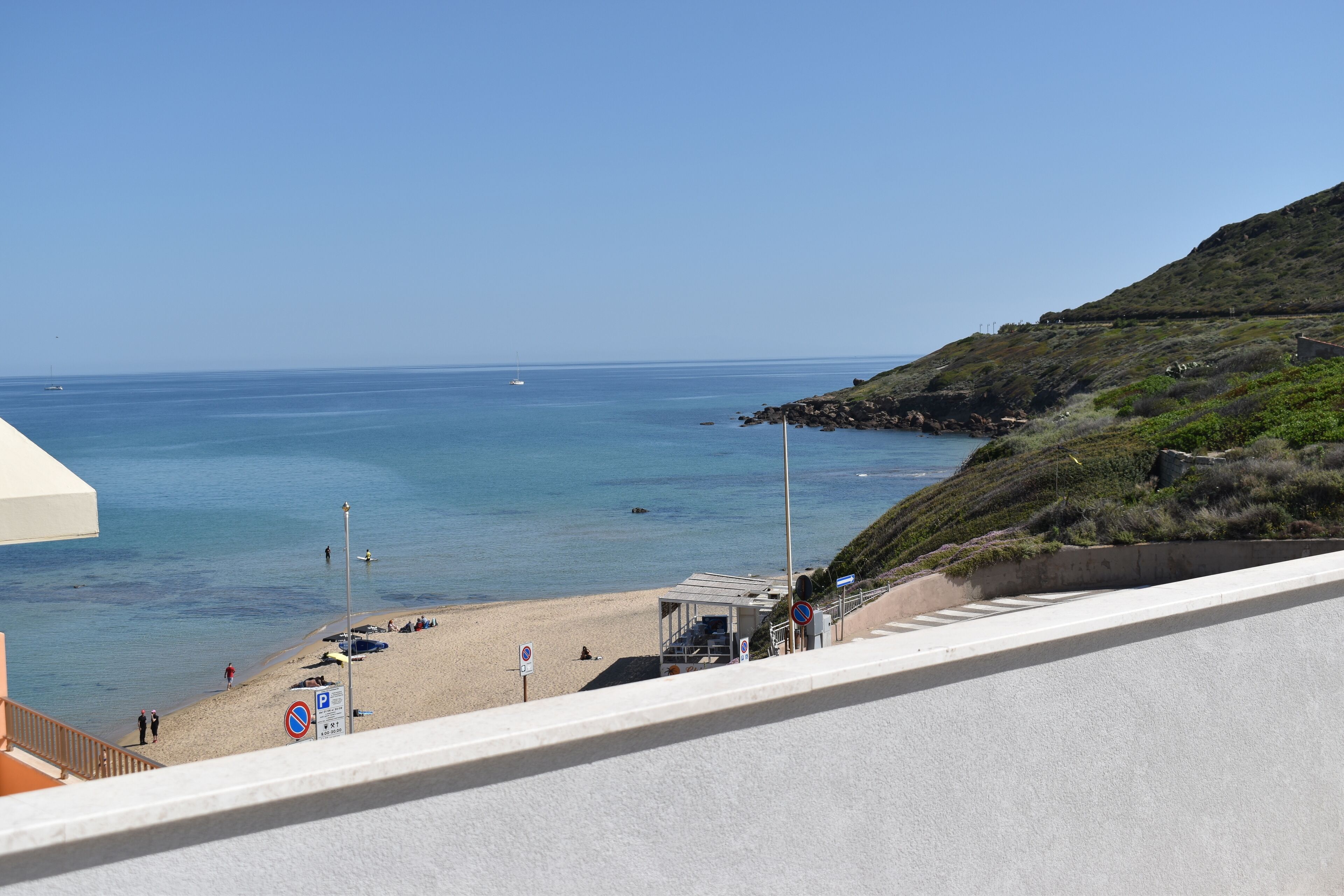 A beach with a clear view of the sea, a lifeguard tower, and a no parking sign.