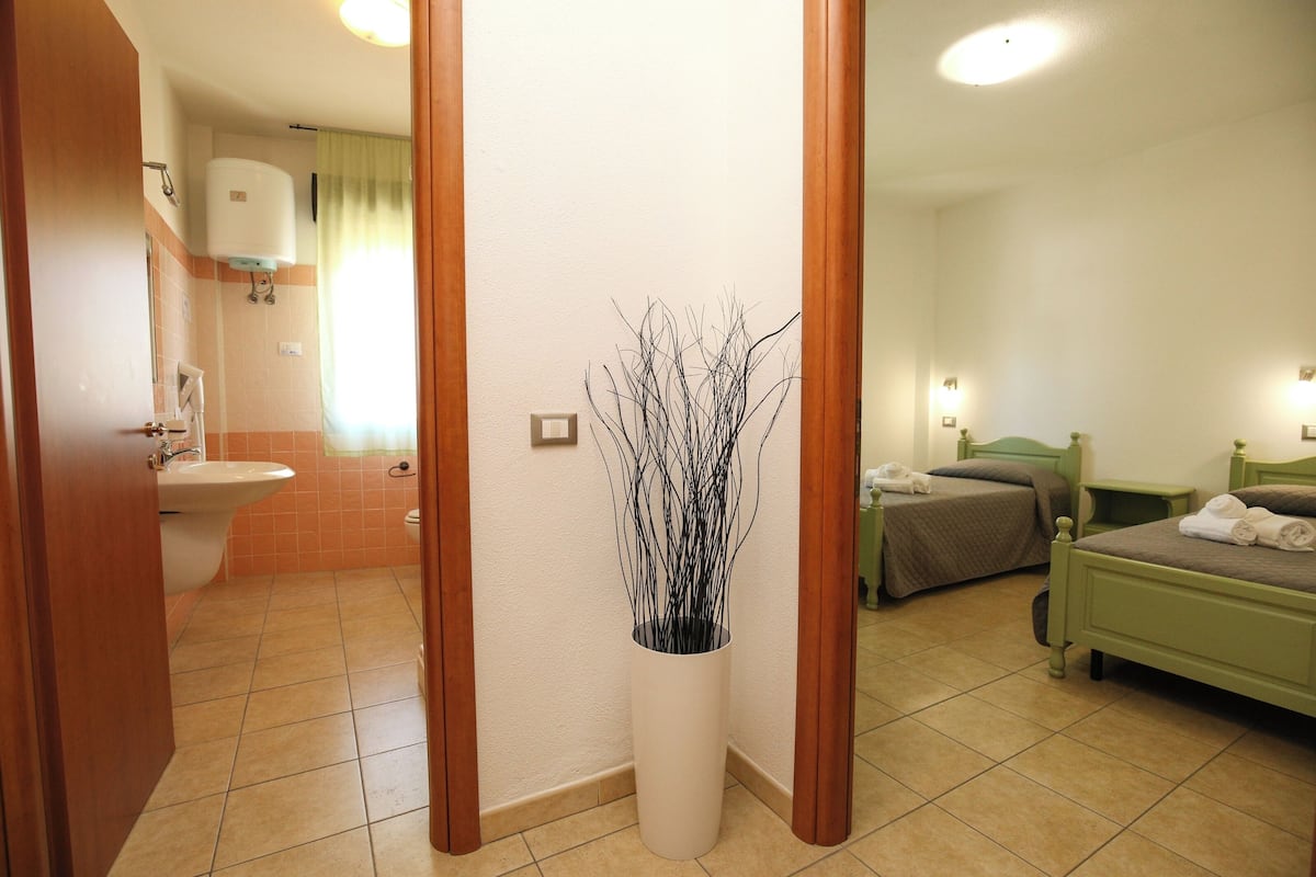 A hotel room with a bathroom, a bed, a bedside table, and a decorative vase.