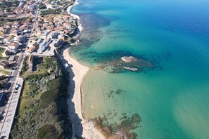 Vista aérea de uma cidade costeira com praia, águas azul-claras e uma mistura de edifícios residenciais e comerciais.