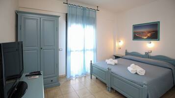 Un dormitorio con cama, televisión, armario y ventana con cortinas.