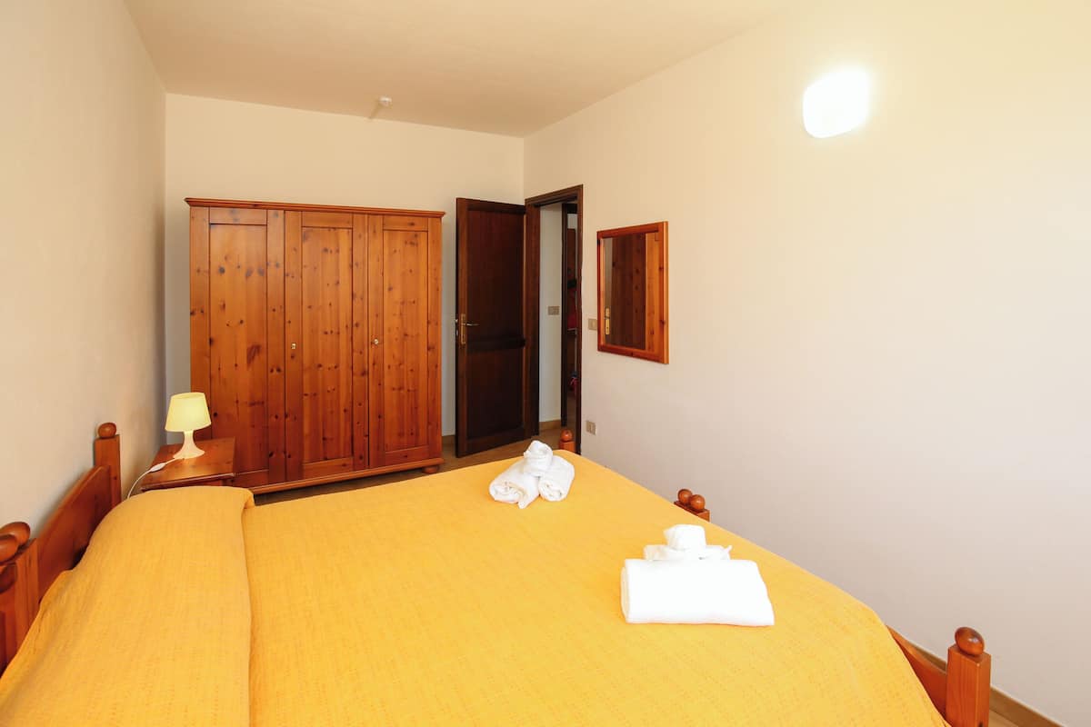 A bedroom with a bed, wooden wardrobe, and a mirror.