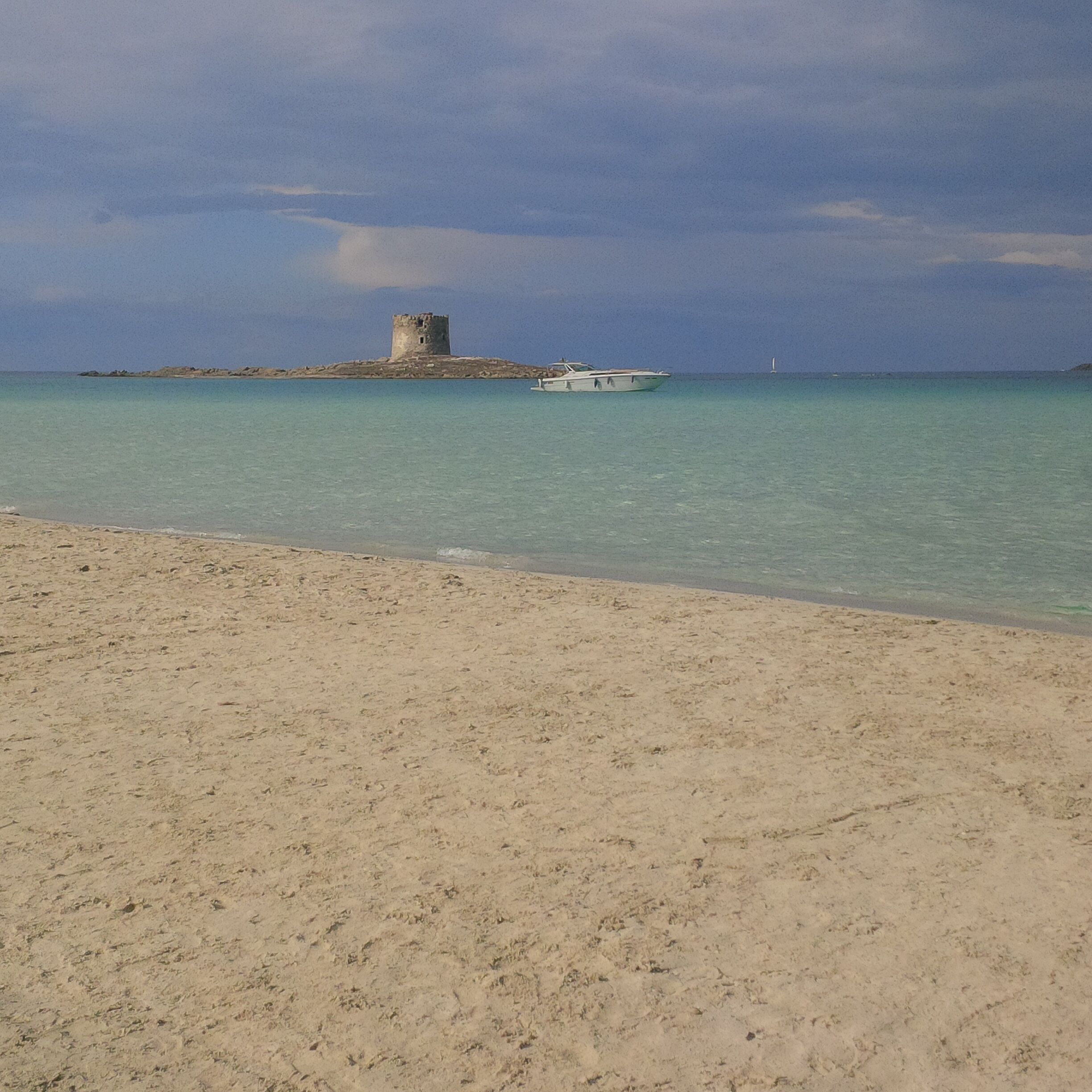 Una playa con arena y una torre a lo lejos.