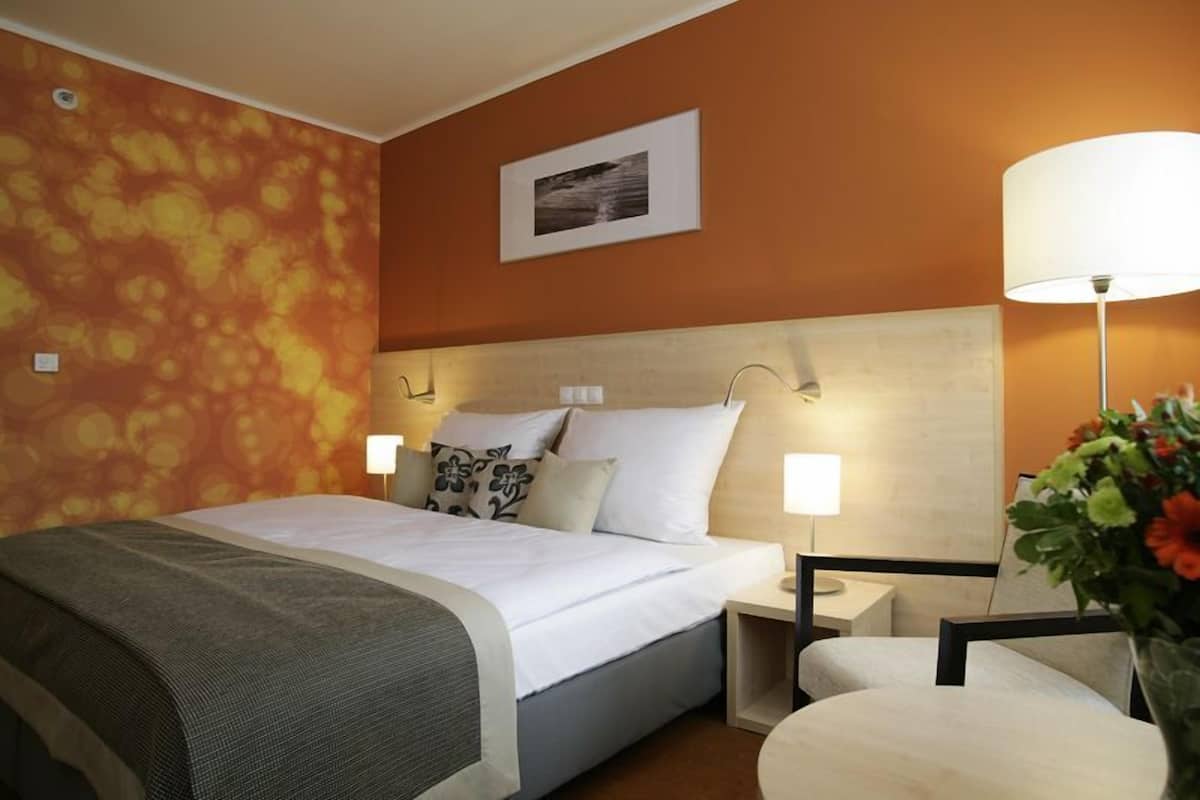 Una habitación de hotel con una cama grande, dos mesitas de noche con lámparas, una silla y una pared con estampado floral.