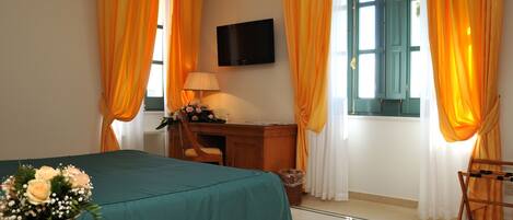 Habitación de hotel con cama, escritorio, silla, televisor y ventana con cortinas.