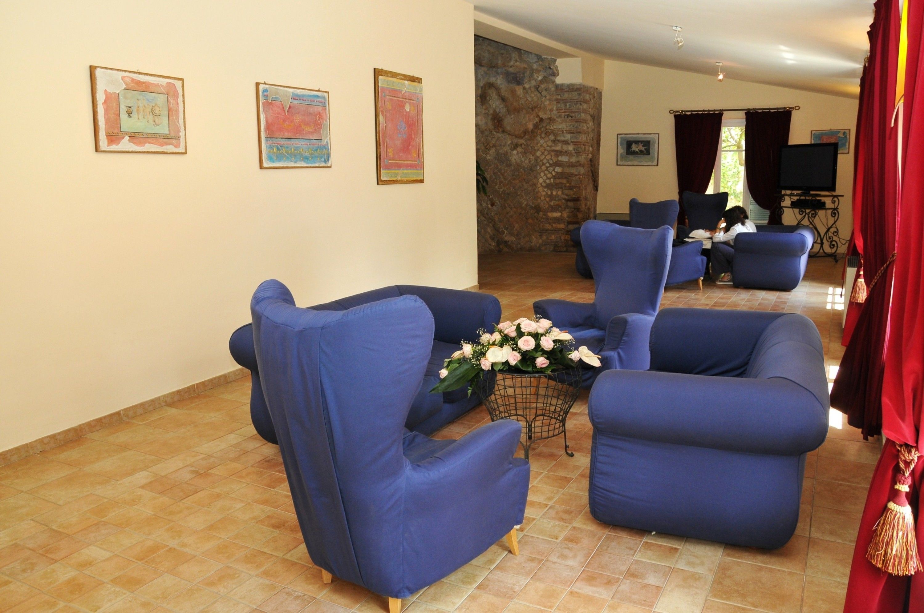 Un salon avec des fauteuils bleus, une table basse ornée de fleurs et un mur en pierre.