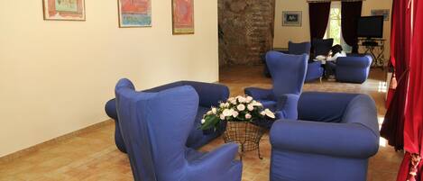 Un salon avec des fauteuils bleus, une table basse ornée de fleurs et un mur en pierre.