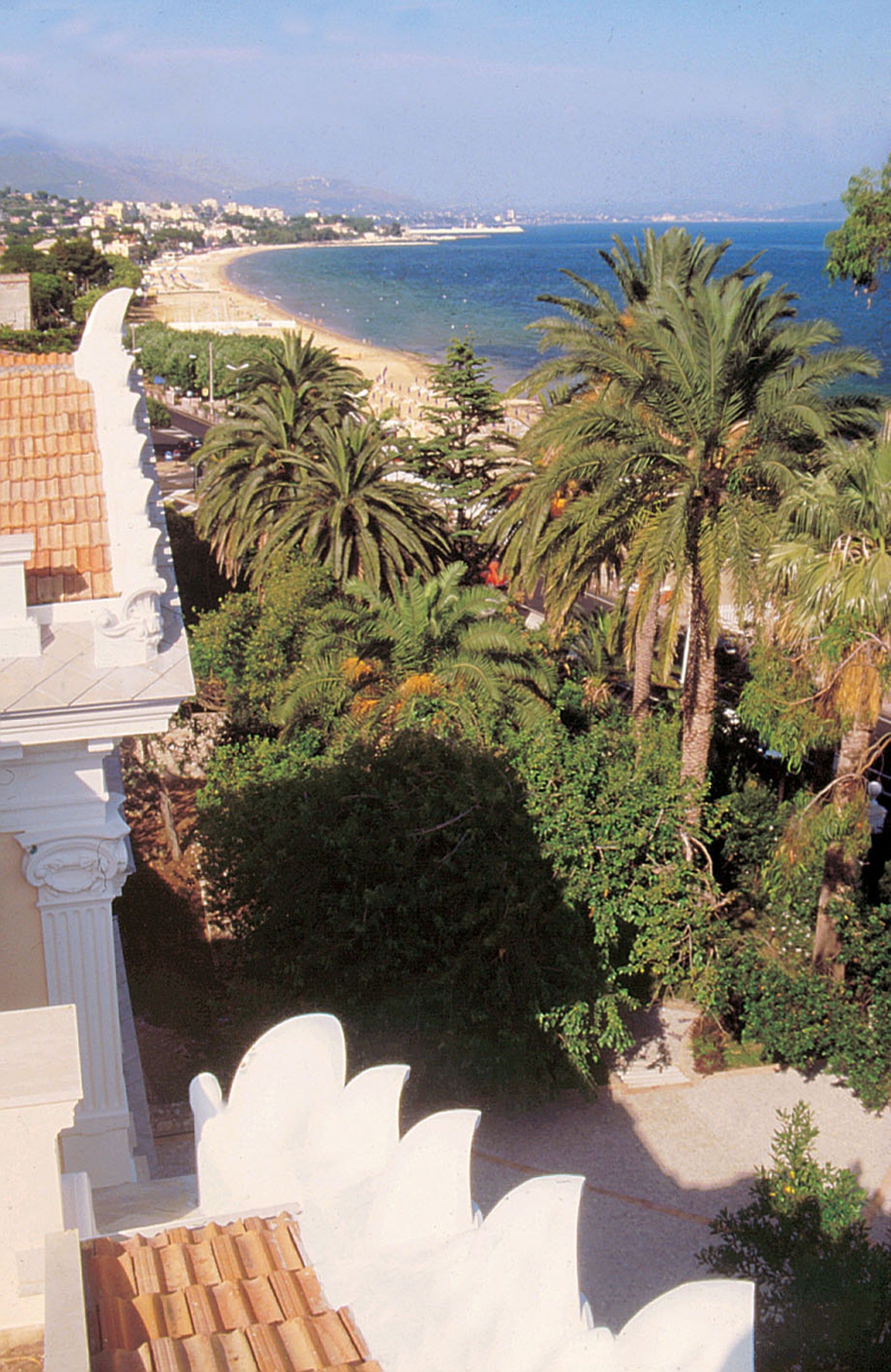 Vista sulla costa con spiaggia, palme e un edificio con tetto in tegole.