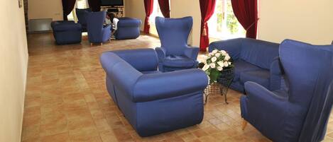 Un amplio salón con sofás y sillones azules, un televisor de pantalla plana y un arreglo floral.