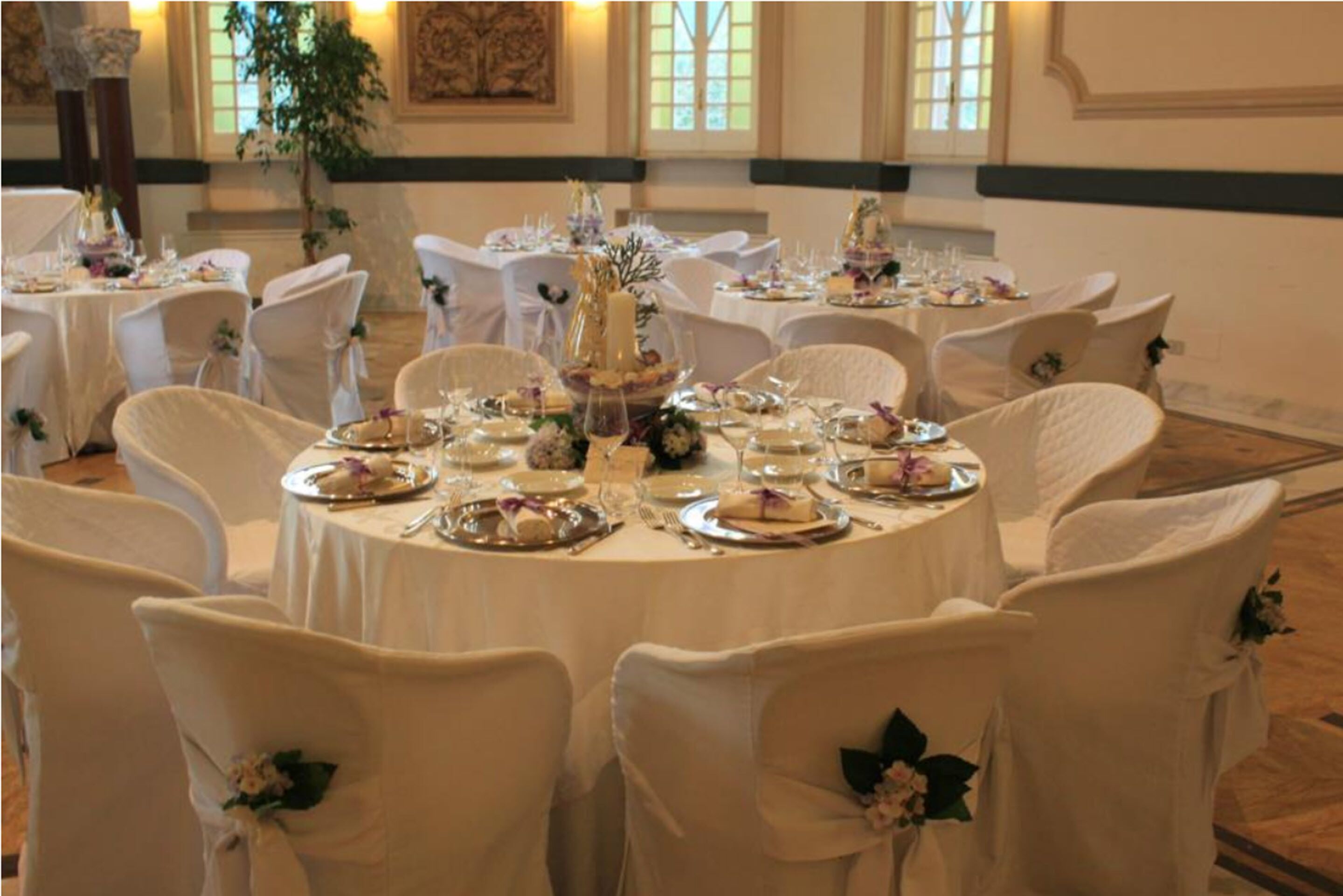 A banquet hall with round tables set for a formal event, adorned with white tablecloths and floral centerpieces.