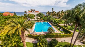 A rectangular pool surrounded by palm trees and a well-manicured lawn, with a building in the background. - Villa Irlanda Grand Hotel (Gaeta)